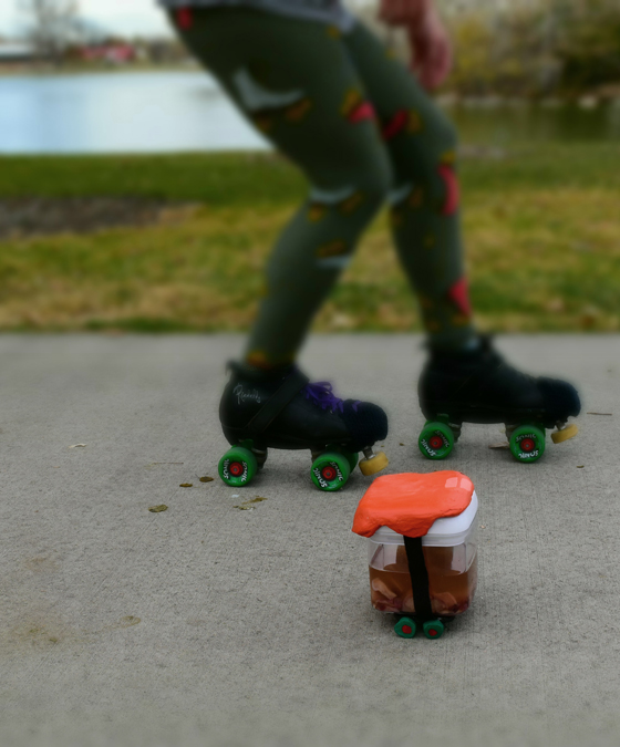 DSC_0178 A uterus in a Tupperware is wearing an orange ceramic helmet and skates. Behind them Chris is skating