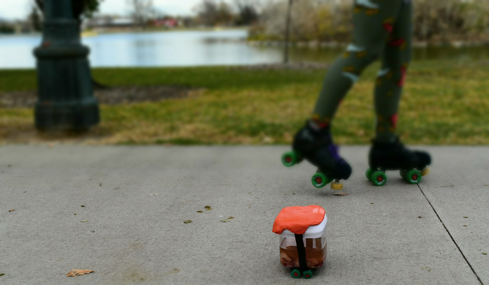 DSC_0180 A uterus in a Tupperware is wearing an orange ceramic helmet and skates. Behind them Chris is skating